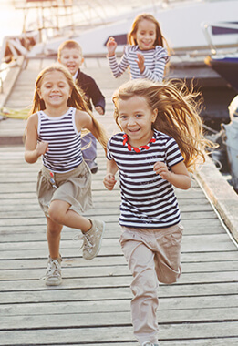 Four children smiling run towards us on a pier