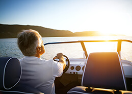 A man is driving a boat with the sunset on the horizon